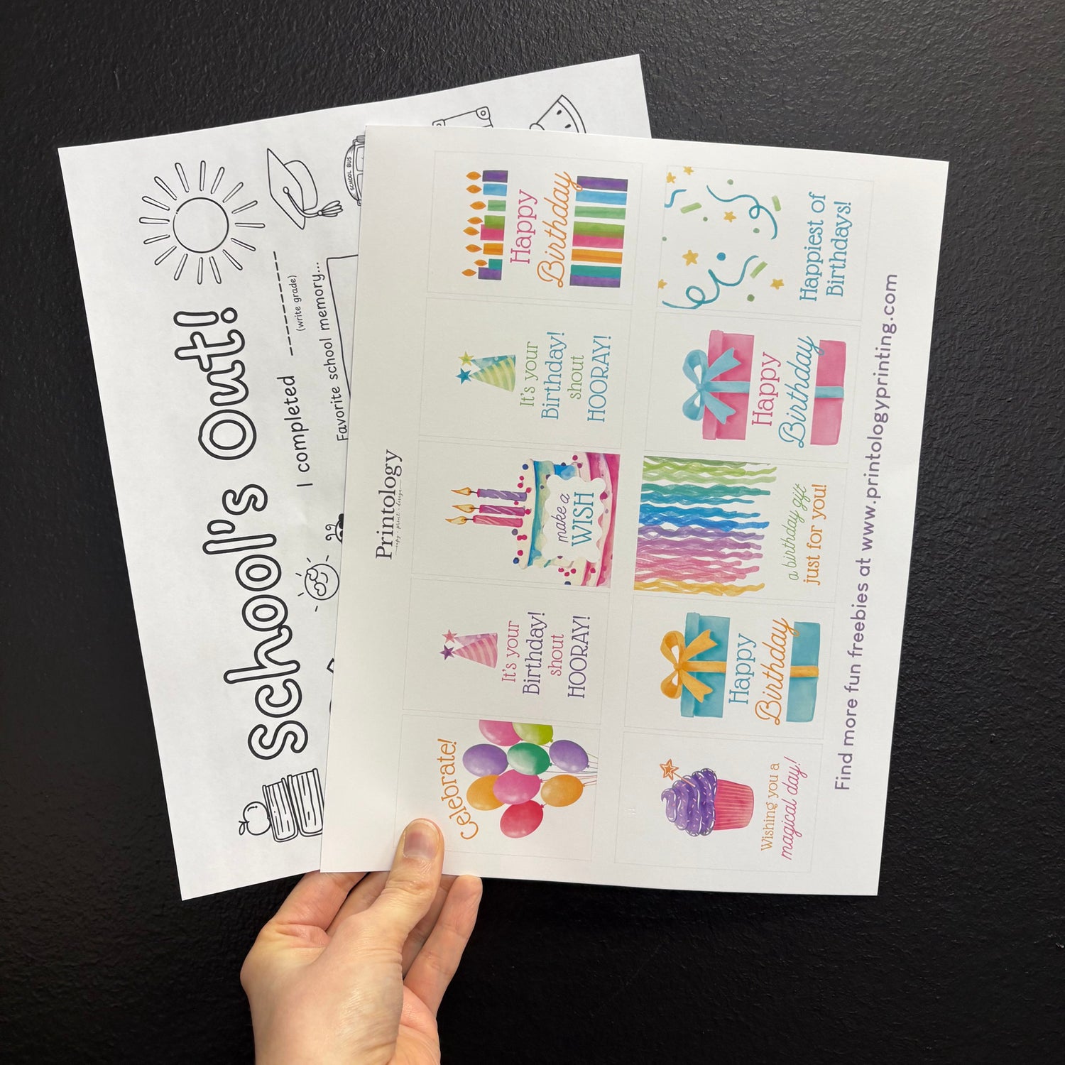 Two sheets of printables held by a hand against a dark background. Black and White versus Color printing. 
