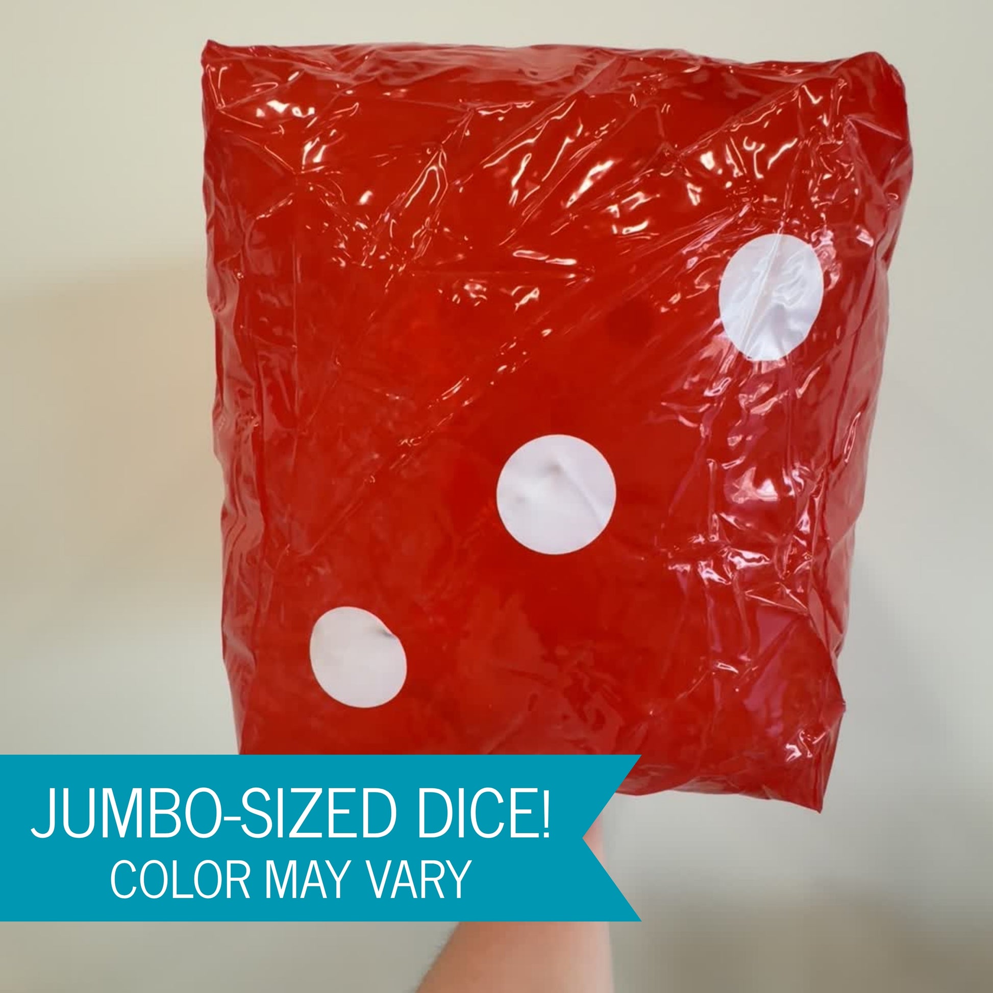 A large glossy inflatable dice with white circular dots, held up by a hand against a plain light background. A blue banner at the bottom reads 'JUMBO-SIZED DICE! COLOR MAY VARY'.