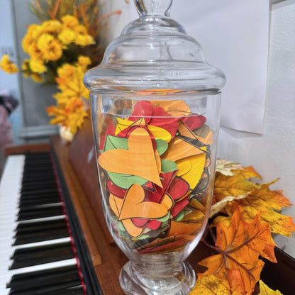 Glass container filled with autumn-themed leaves on a piano