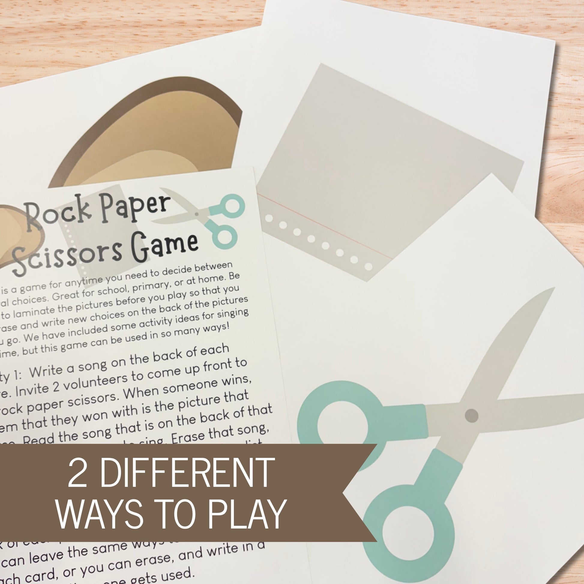 Rock Paper Scissors Game printed on a sheet of paper, shown on a light wood surface with a brown banner overlay reading '2 DIFFERENT WAYS TO PLAY'.