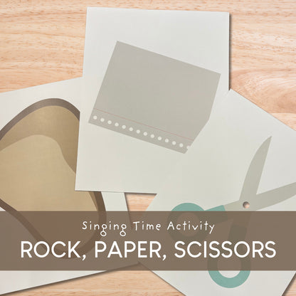 Singing Time Activity Rock, Paper, Scissors game cards laid out on a light wood surface, with a brown banner across the bottom reading 'Singing Time Activity ROCK, PAPER, SCISSORS'.