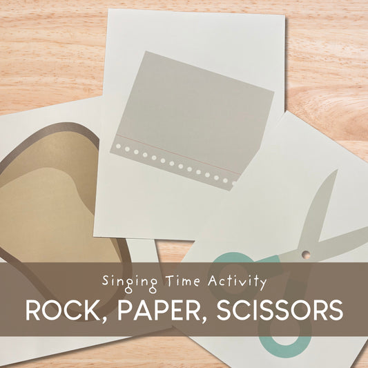 Singing Time Activity Rock, Paper, Scissors game cards laid out on a light wood surface, with a brown banner across the bottom reading 'Singing Time Activity ROCK, PAPER, SCISSORS'.