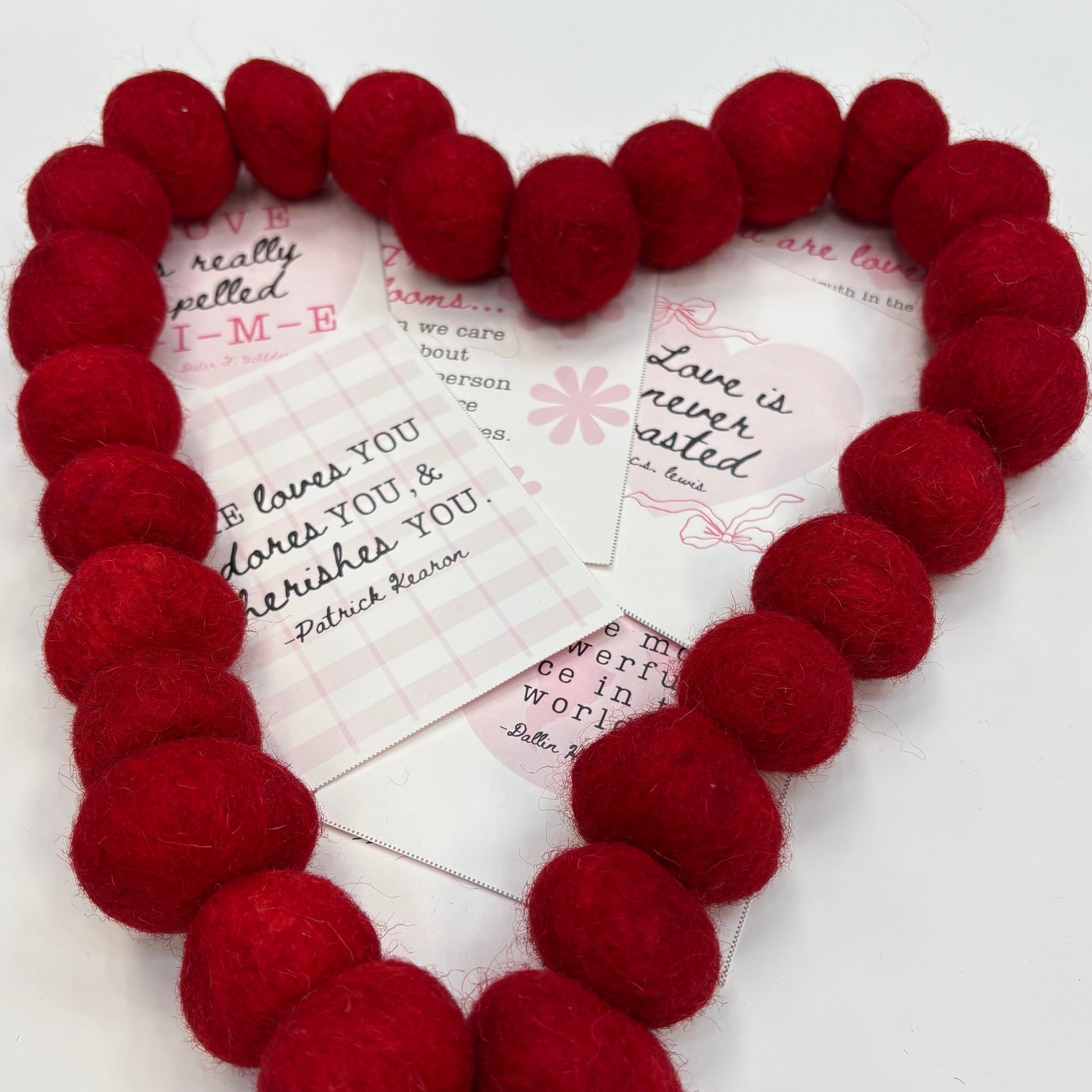 Red heart-shaped wreath with Valentine cards underneath on a white background