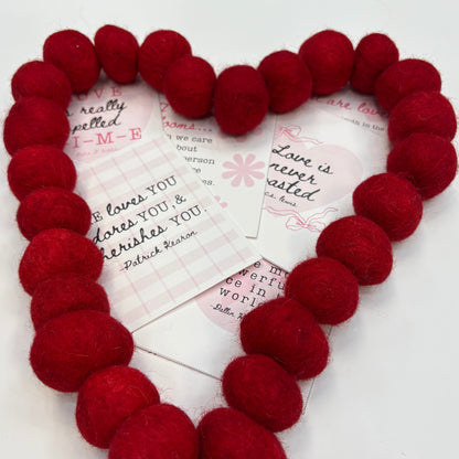 Red heart-shaped wreath with Valentine cards underneath on a white background